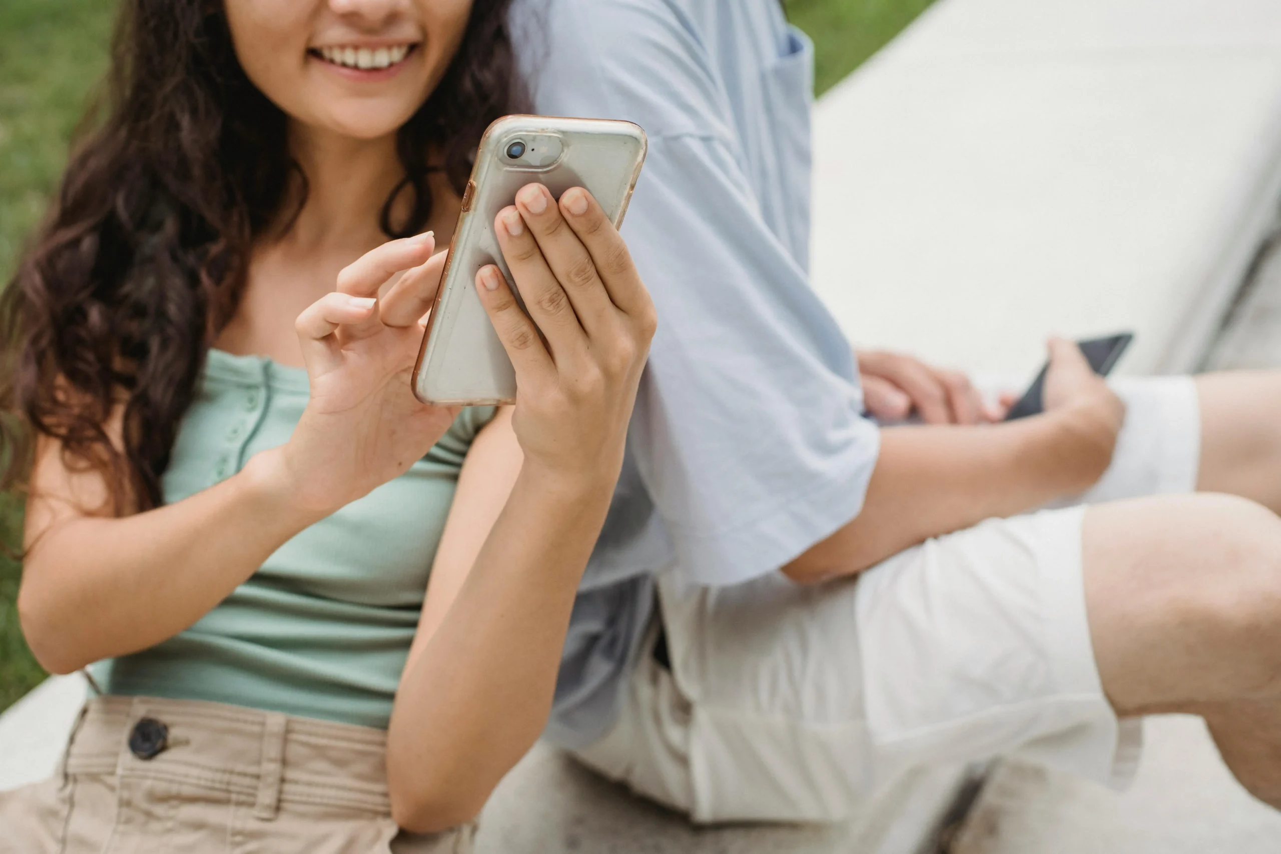 Mulher mostrando conteúdo no celular para um homem ao lado e sorrindo.